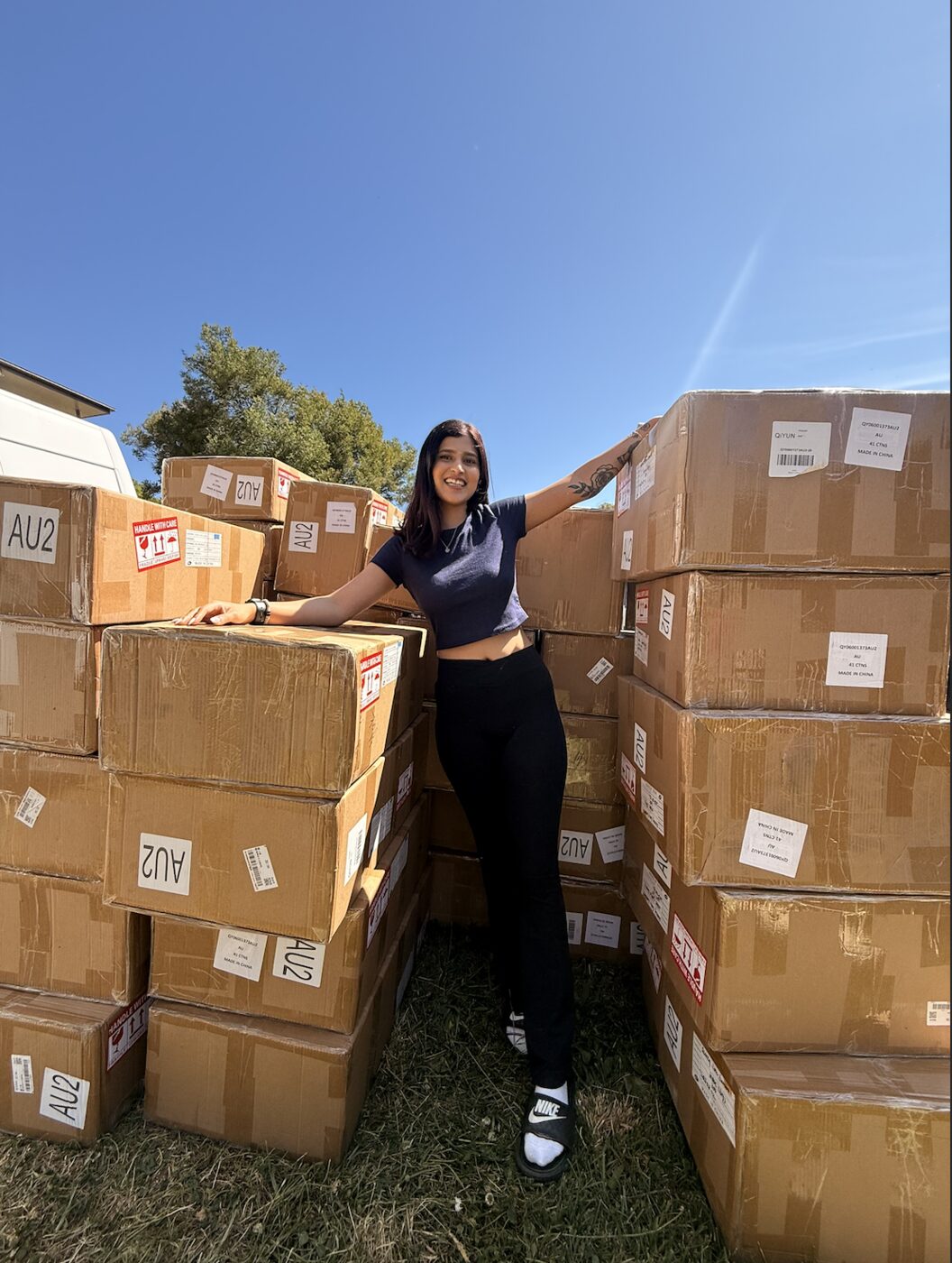 Krish Waje standing among shipping boxes of her eCommerce inventory